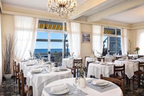 A cozy seaside restaurant with elegant white tablecloths, wooden chairs, and large windows offering a serene ocean view, perfect for a romantic dinner or a relaxing lunch by the sea.