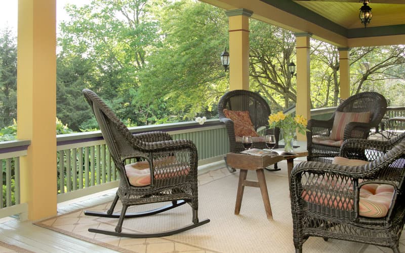 A serene porch with wicker furniture, vibrant cushions, and lush greenery offers a tranquil retreat for relaxation and leisurely sipping wine.