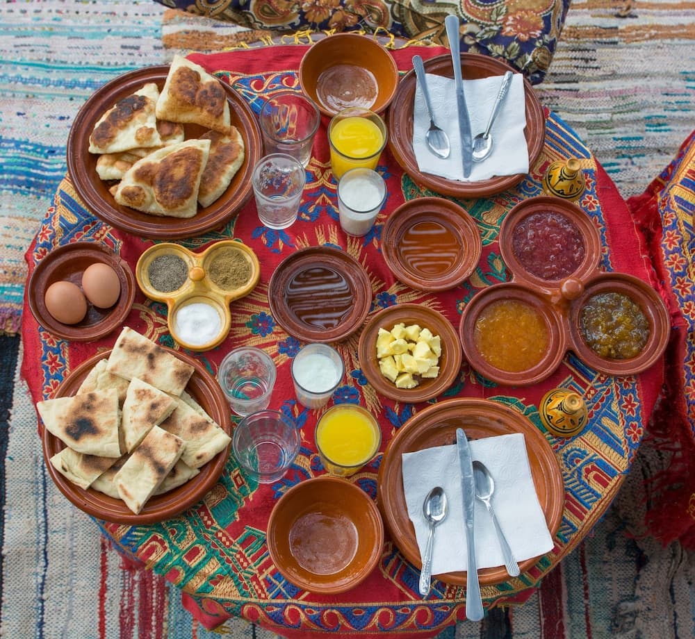 A vibrant, colorful tablecloth adorned with traditional Middle Eastern breakfast items like flatbread, eggs, jams, and spices creates an inviting and authentic dining experience perfect for cultural immersion travelers.