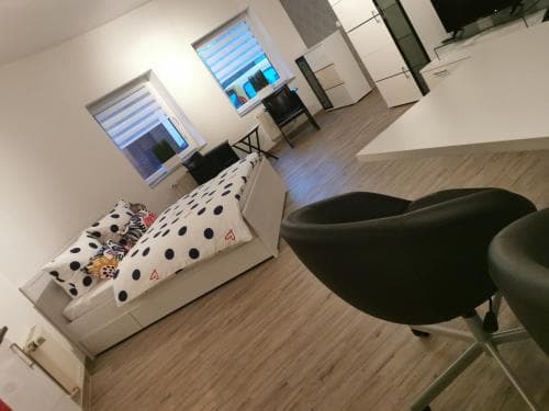 A cozy modern apartment features a stylish living area with a polka-dot sofa, sleek black chairs, wooden flooring, and large windows, ideal for travelers seeking comfort and contemporary design in their accommodation.