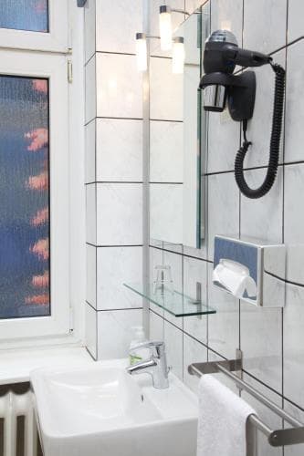 A modern hotel bathroom features a sleek sink, mounted hairdryer, and frosted window with a serene sunset view, ideal for travelers seeking comfort and style.