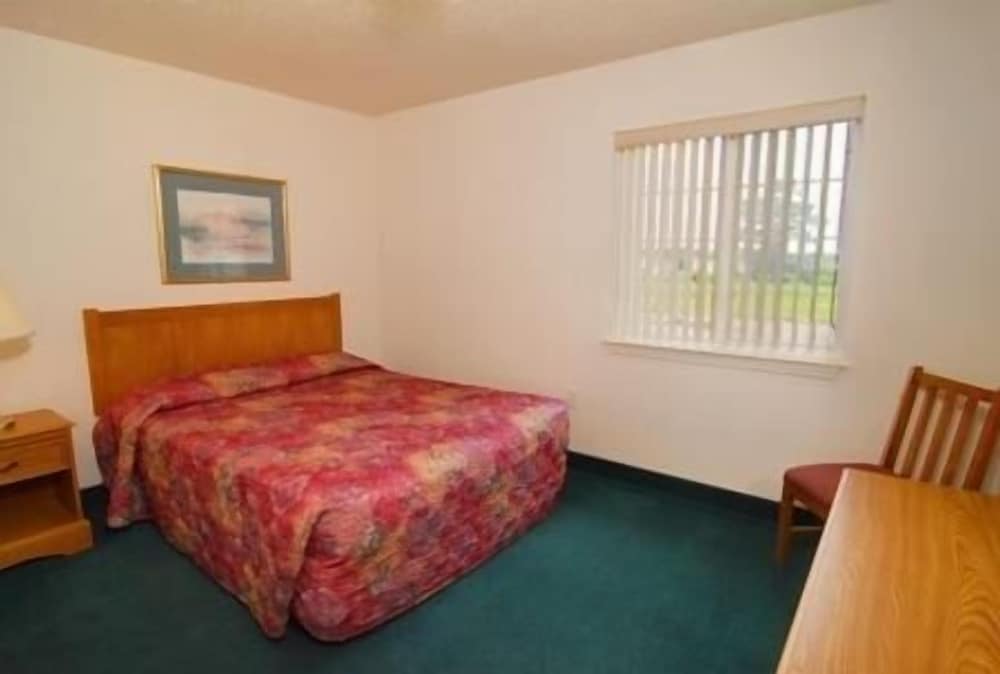 A cozy motel room features a neatly made bed with a floral comforter, wooden furniture, and a window with blinds, ideal for travelers seeking a simple and comfortable stay.