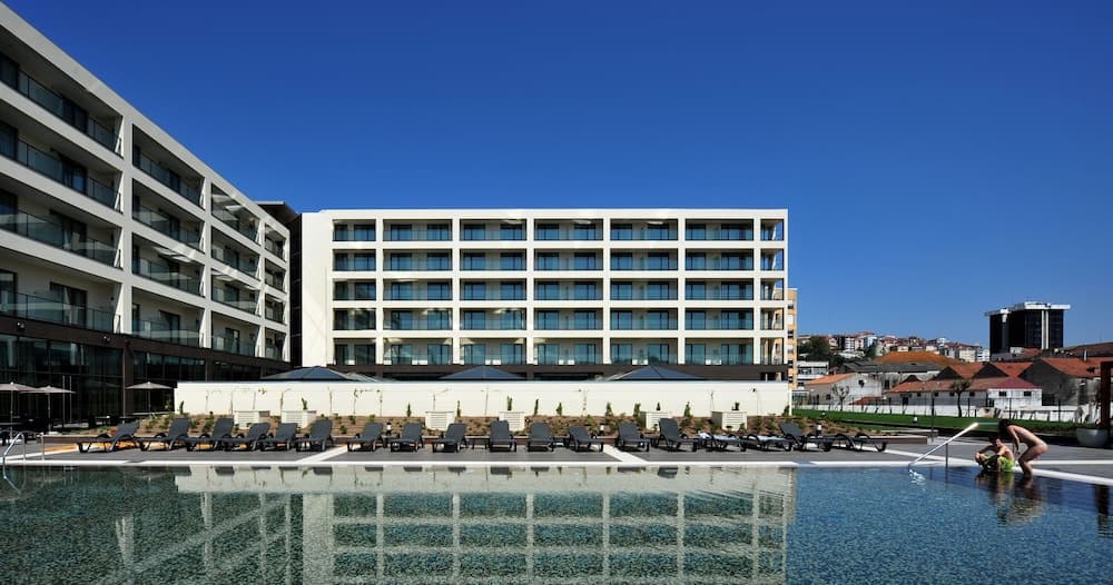 A serene hotel resort features a large swimming pool lined with lounge chairs under a clear blue sky, ideal for travelers seeking relaxation and luxury accommodations.