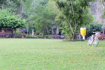 A serene park scene features a lush green lawn, bicycles parked nearby, and a giant beer mug sculpture, ideal for a relaxing outdoor picnic or leisurely bike ride.