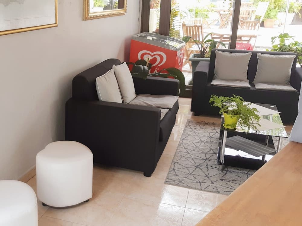 A cozy indoor lounge area features black sofas with gray cushions, a glass coffee table adorned with a green plant, and a bright patio view through large windows, ideal for travelers seeking a relaxing retreat space.