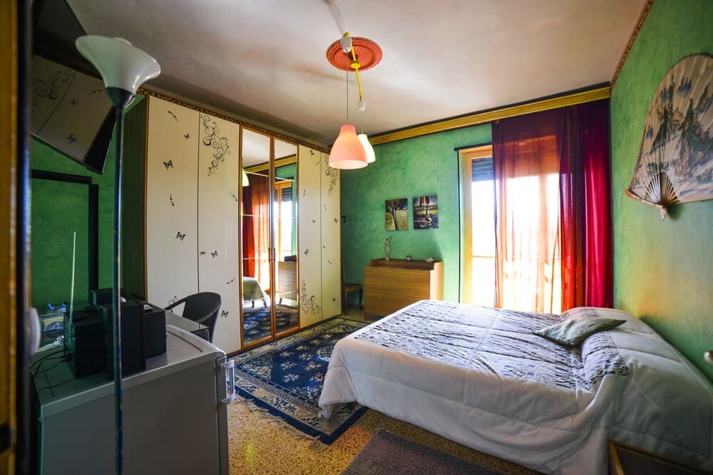 A cozy bedroom with green walls, red curtains, and eclectic decor offers a serene retreat, ideal for travelers seeking a charming and personalized accommodation experience.