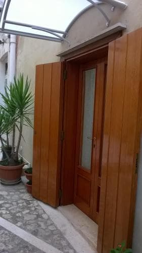 A cozy courtyard entrance featuring a wooden door with glass panels, flanked by potted plants, evokes a serene Mediterranean ambiance ideal for travelers seeking quaint accommodations.