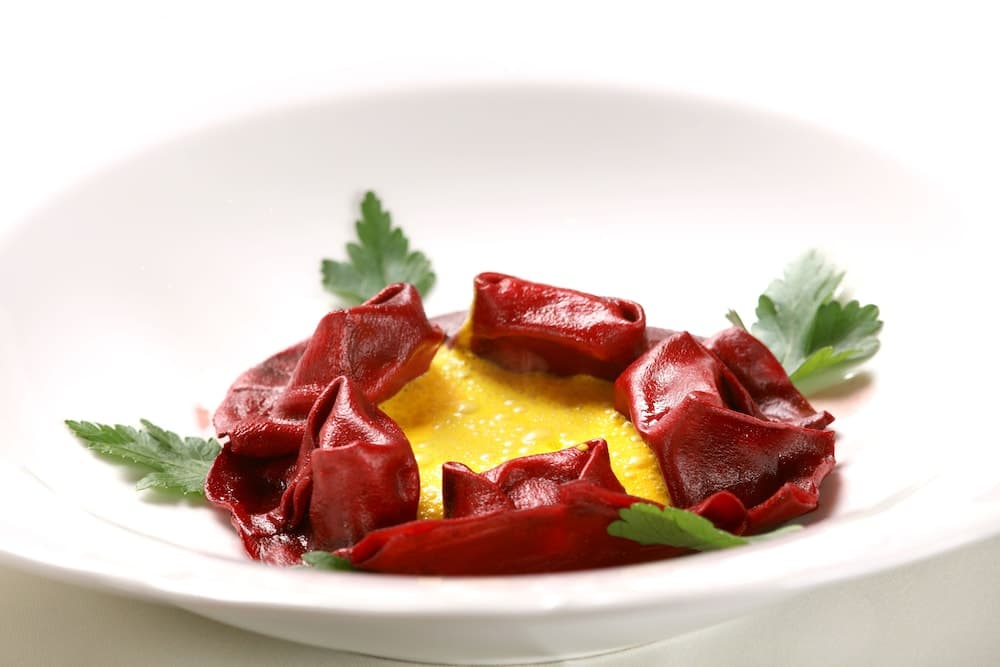 A beautifully plated dish featuring vibrant red pasta encircling a golden yolk center, garnished with fresh green herbs, evokes an elegant dining experience ideal for culinary enthusiasts exploring gourmet cuisine.