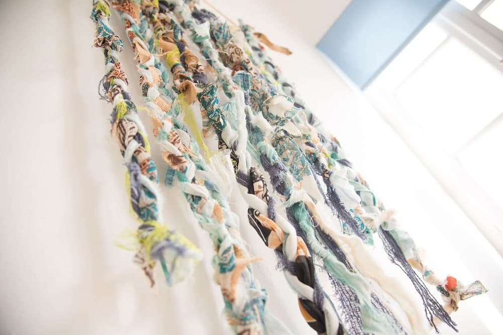 A vibrant textile art installation hangs gracefully in a well-lit indoor space, creating an inviting and creative atmosphere ideal for travelers seeking unique cultural experiences and artistic inspiration.