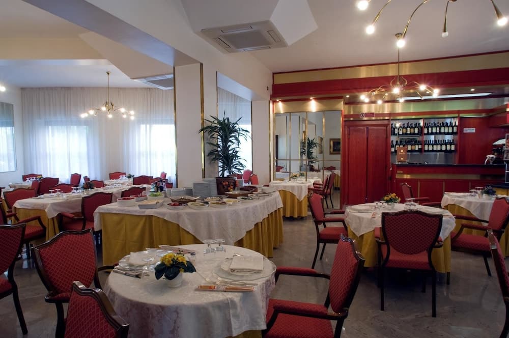 A cozy restaurant interior features tables set for dining under warm chandeliers, with red chairs, white tablecloths, and a bar area stocked with bottles, ideal for travelers seeking a comfortable dining experience.