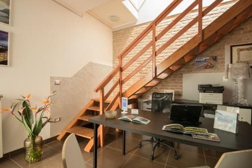A cozy office space with a wooden staircase, brick wall, and modern desk setup exudes a professional yet inviting atmosphere, ideal for travelers seeking a productive work environment during their stay.