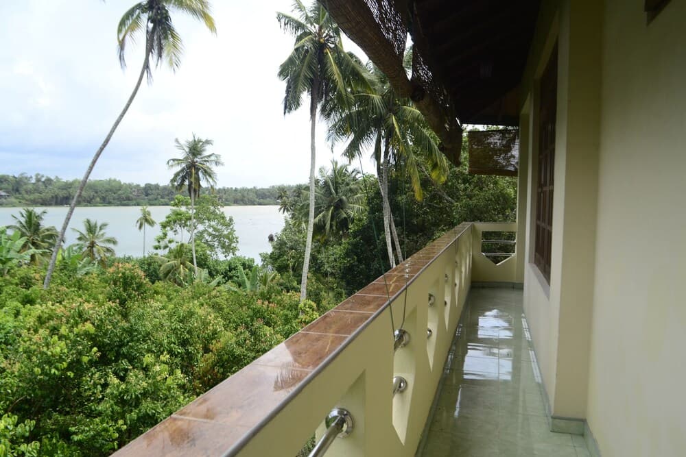 A serene balcony overlooks lush tropical greenery and a tranquil water body, ideal for a relaxing vacation retreat.