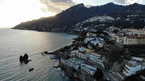 A picturesque coastal town nestled against towering mountains bathes in the warm glow of sunset, featuring charming white buildings and rocky outcrops, ideal for travelers seeking serene seaside retreats.