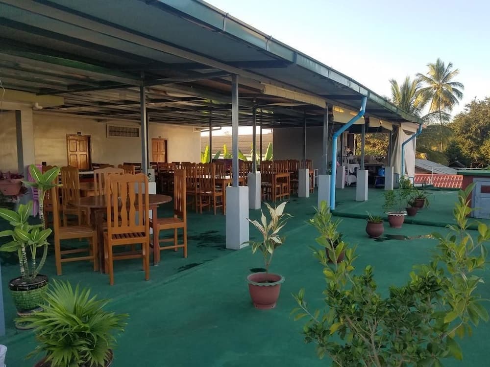 A serene outdoor dining area with wooden tables and chairs under a shaded roof, surrounded by lush greenery and potted plants, ideal for travelers seeking a tranquil tropical retreat.