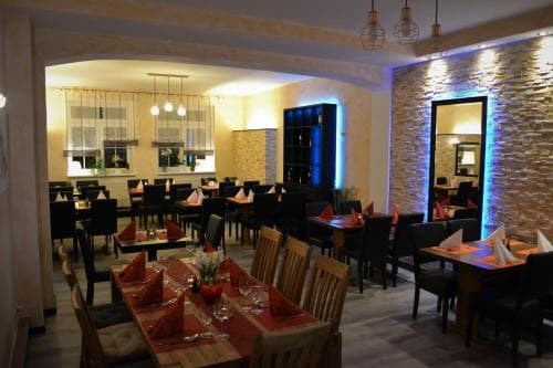 A cozy restaurant interior with warmly lit tables set for dining, featuring rustic wooden chairs, red napkins, and ambient lighting, ideal for travelers seeking a comfortable dining experience.