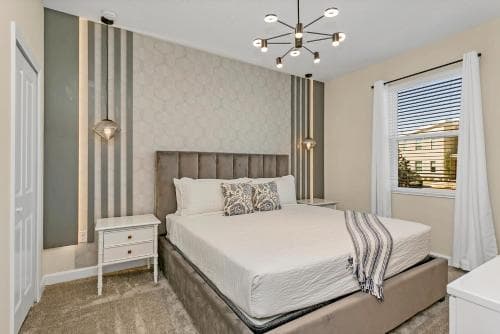 A cozy bedroom with modern decor, featuring a neatly made bed, stylish bedside tables, and a contemporary chandelier, ideal for travelers seeking comfort in a boutique hotel setting.