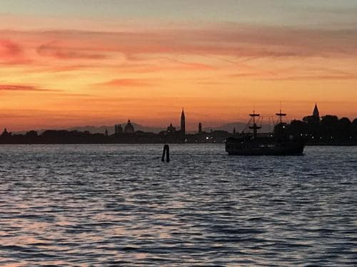 A serene sunset over a historic waterfront cityscape reflects on calm waters, featuring silhouetted ships and iconic spires, ideal for romantic getaways or cultural exploration.