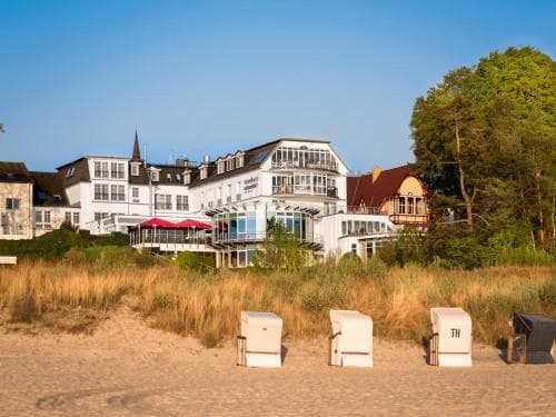 A serene beachfront scene features traditional beach chairs on sandy shores, with charming seaside buildings and lush greenery in the background, ideal for a relaxing coastal getaway.