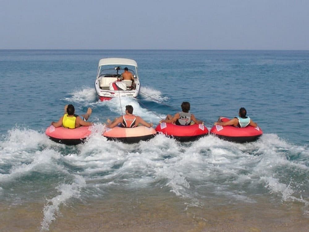 Enjoy an exhilarating beach adventure as friends tube behind a speedboat on vibrant inner tubes, perfect for summer vacation thrills.