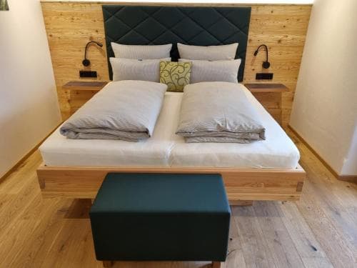 A cozy hotel room features a modern wooden bed with plush bedding, black leather accents, and warm lighting, ideal for travelers seeking comfort and style.