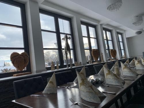 A cozy restaurant with large windows offering scenic views, set tables adorned with artistic napkin folds, and heart-shaped decor, perfect for a romantic dining experience or a special occasion.