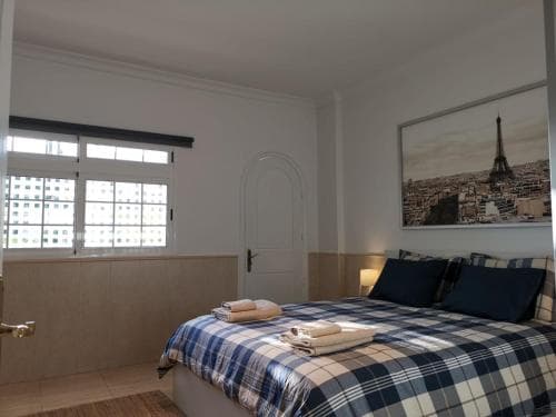 A cozy bedroom with a neatly made plaid bed, Paris-themed artwork, and soft natural light filtering through a window, ideal for travelers seeking a serene and stylish accommodation.