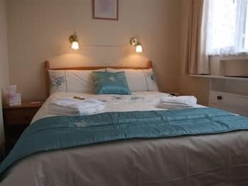 A cozy hotel room features a neatly made bed with turquoise bedding, soft lighting from wall-mounted lamps, and a serene atmosphere ideal for relaxation during a travel getaway.