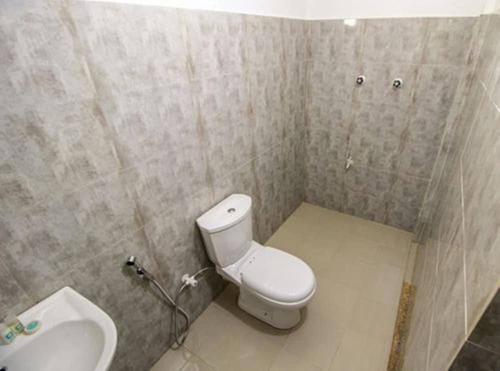 A compact bathroom with tiled walls and floor features a toilet, sink, and handheld shower, ideal for travelers seeking basic amenities in a functional space.