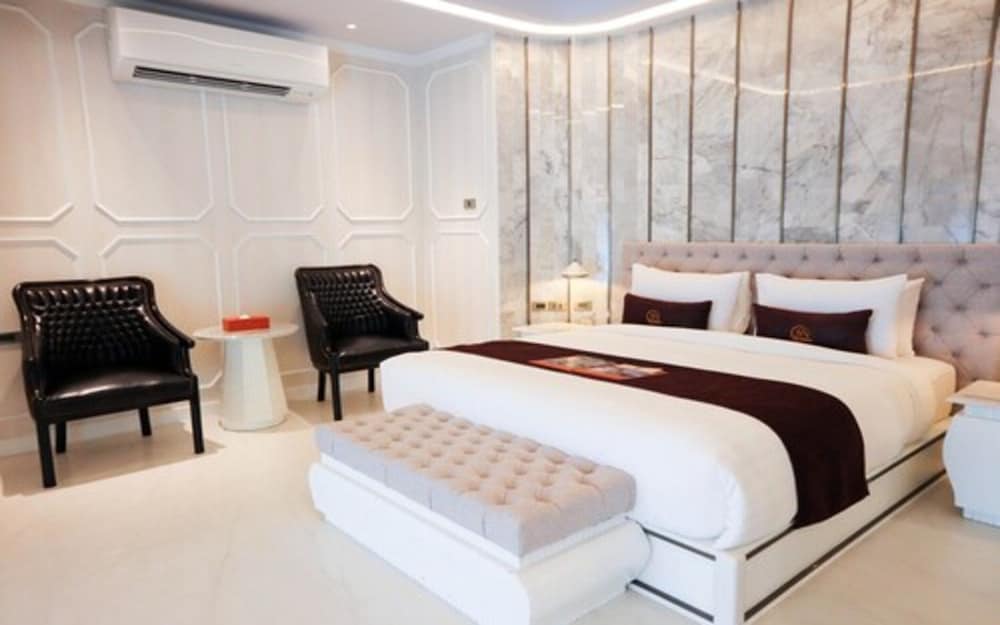 A luxurious hotel bedroom features a cozy king-sized bed with plush bedding, elegant black leather armchairs, and a modern marble accent wall, ideal for travelers seeking comfort and style during their stay.