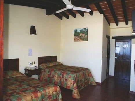 A cozy hotel room with vibrant floral bedding, wooden beams, and tropical artwork creates a warm, inviting atmosphere ideal for travelers seeking comfort in a budget-friendly accommodation.