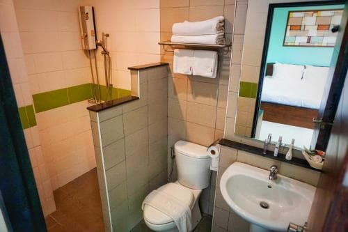 A compact hotel bathroom features a tiled shower area, white toilet, sink, and mirror, creating a clean and functional space ideal for travelers seeking basic amenities.
