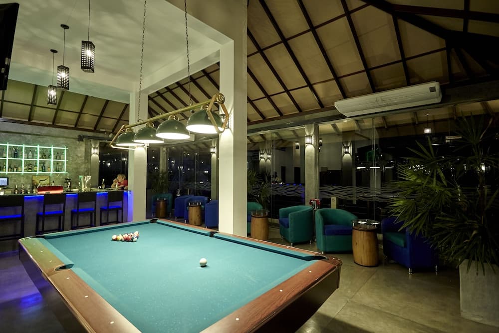 A cozy lounge area featuring a pool table under warm lighting, surrounded by plush seating and a bar, ideal for travelers seeking relaxation and entertainment in a stylish indoor setting.