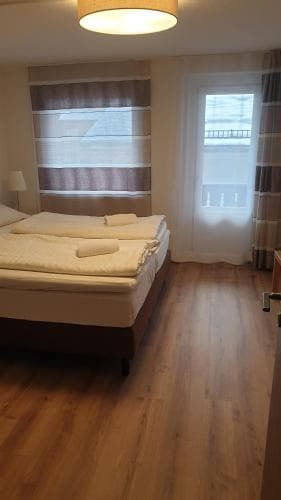 A cozy hotel room with wooden flooring, neatly made bed, soft lighting, and balcony view offers a comfortable stay for travelers seeking relaxation.