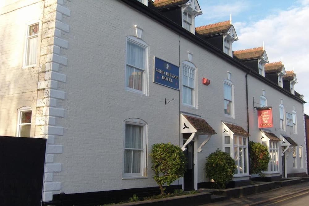 A charming white brick hotel with dormer windows and greenery exudes a cozy, welcoming atmosphere ideal for travelers seeking a quaint stay in a picturesque town setting.