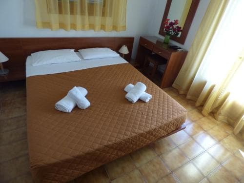 A cozy hotel room with a neatly made bed adorned with folded towels, warm yellow curtains, tiled flooring, and a wooden desk, ideal for travelers seeking comfort and simplicity.