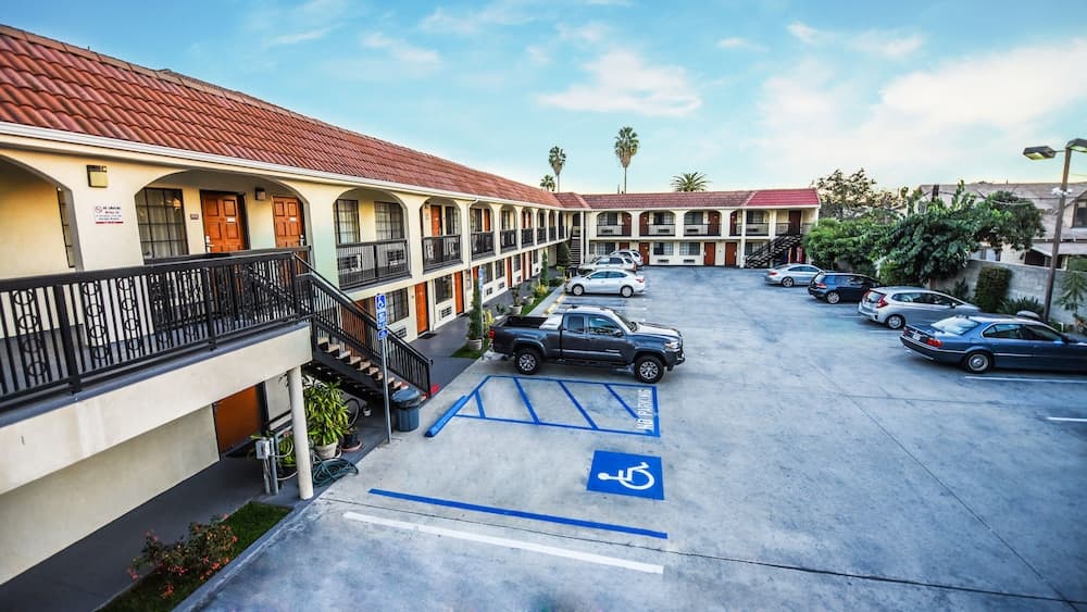 A sunny courtyard of a motel features parked cars, accessible parking spaces, palm trees, and a welcoming atmosphere ideal for travelers seeking convenient accommodations.