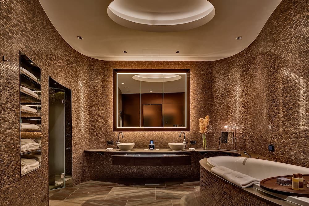 A luxurious spa bathroom with warm-toned mosaic walls, a large mirror, dual sinks, and a cozy bathtub creates an inviting and serene atmosphere ideal for relaxation and wellness retreats.