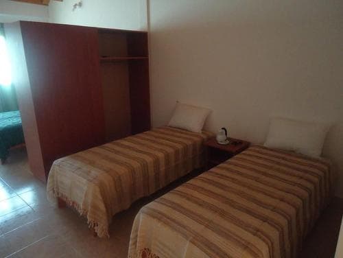 A cozy budget-friendly hotel room features two neatly made single beds with striped blankets, a simple wardrobe, and a small bedside table with a lamp, ideal for travelers seeking basic accommodations.