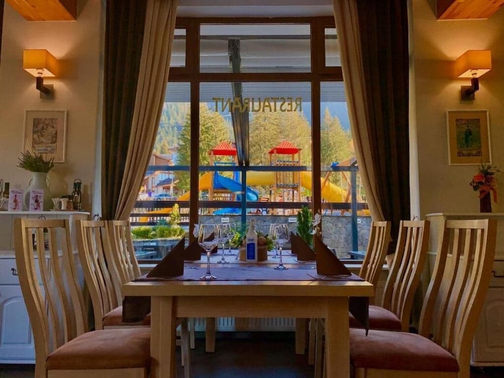 A cozy restaurant interior with wooden furniture and warm lighting overlooks a vibrant playground surrounded by lush greenery, ideal for family-friendly dining experiences.