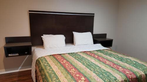 A cozy hotel room features a neatly made bed with a vibrant patterned comforter, sleek black floating nightstands, and a minimalist design, ideal for travelers seeking comfort and simplicity.