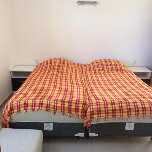 A cozy bedroom features a neatly made bed with a vibrant yellow and red plaid blanket, flanked by simple nightstands, ideal for travelers seeking a comfortable and budget-friendly accommodation.
