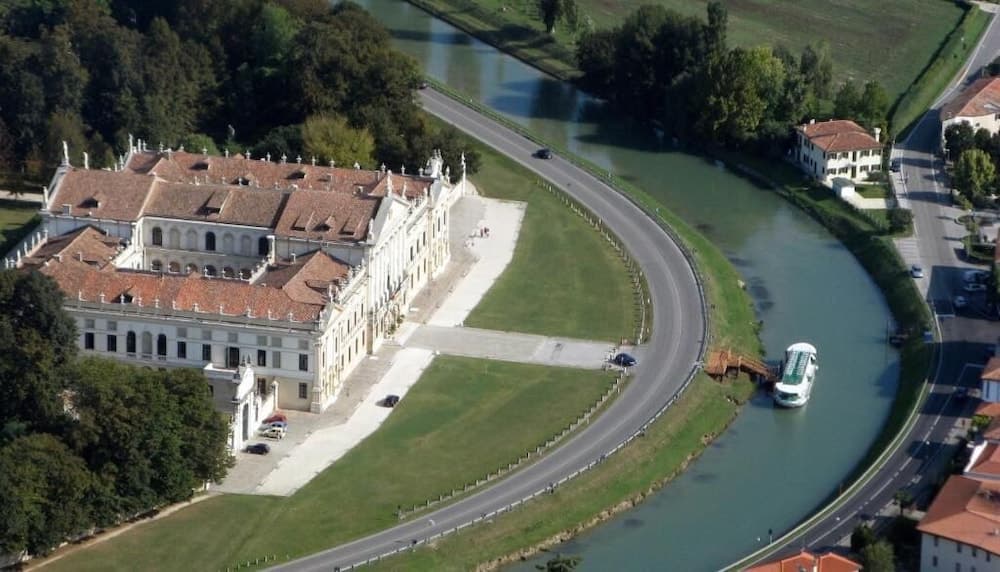 An aerial view captures the serene grandeur of a historic mansion beside a winding river, surrounded by lush greenery, ideal for cultural heritage tourism and scenic photography.