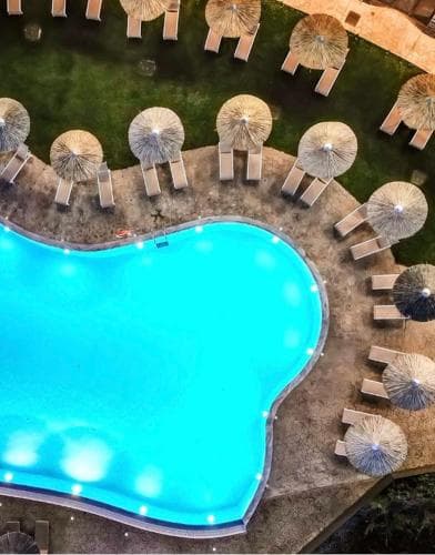 An aerial view captures a vibrant resort pool surrounded by neatly arranged lounge chairs and straw umbrellas, evoking a serene and luxurious vacation atmosphere ideal for relaxation and leisure.