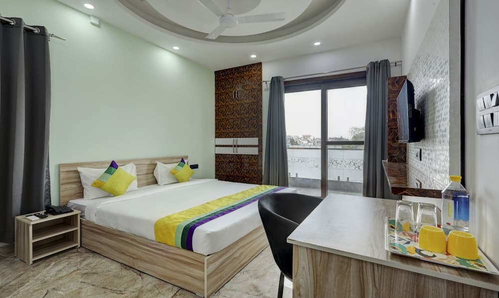 A cozy hotel room with a neatly made bed adorned in vibrant yellow and purple accents, a modern desk setup, and a serene balcony view, ideal for travelers seeking comfort and convenience.