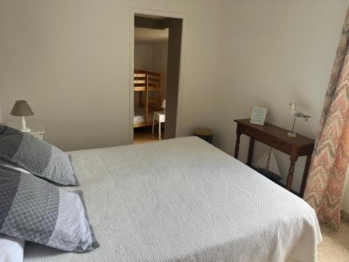 A cozy bedroom with a neatly made bed, wooden furniture, and bunk beds in the background offers a comfortable stay for travelers seeking a quiet retreat.