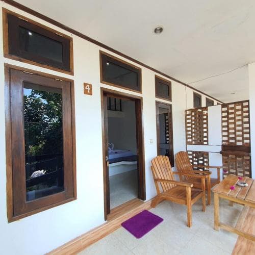 A cozy hotel corridor with open doors revealing rooms, wooden chairs, and tables invites travelers seeking relaxation in a serene tropical setting.