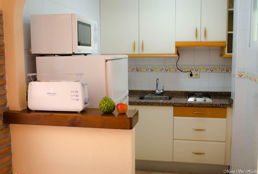 A cozy kitchenette with white cabinetry, a microwave, toaster, and fresh fruits on a wooden counter, exudes a warm and inviting atmosphere ideal for travelers seeking a self-catering accommodation experience.