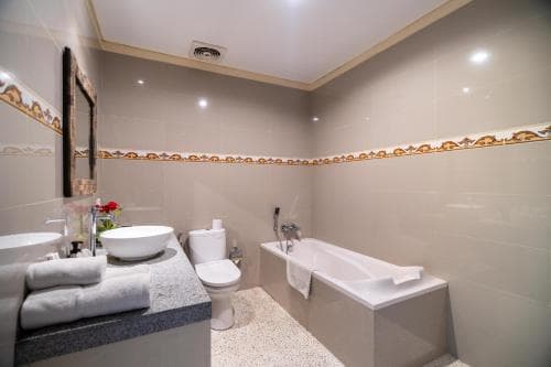 A modern bathroom with beige tiled walls, a bathtub, double sinks, and neatly folded towels creates a serene and luxurious atmosphere ideal for hotel or vacation rental listings.