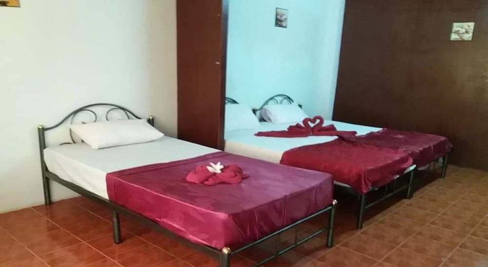 A cozy hotel room features two neatly arranged beds with vibrant red accents and decorative towel swans, ideal for travelers seeking a comfortable and budget-friendly stay.