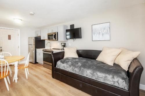 A cozy studio apartment features a modern kitchenette, dining area, and a plush daybed in a warm, inviting space ideal for solo travelers seeking comfort and convenience.